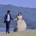 A couple in elegant wedding attire walking hand in hand by a picturesque riverbank in Una, India.